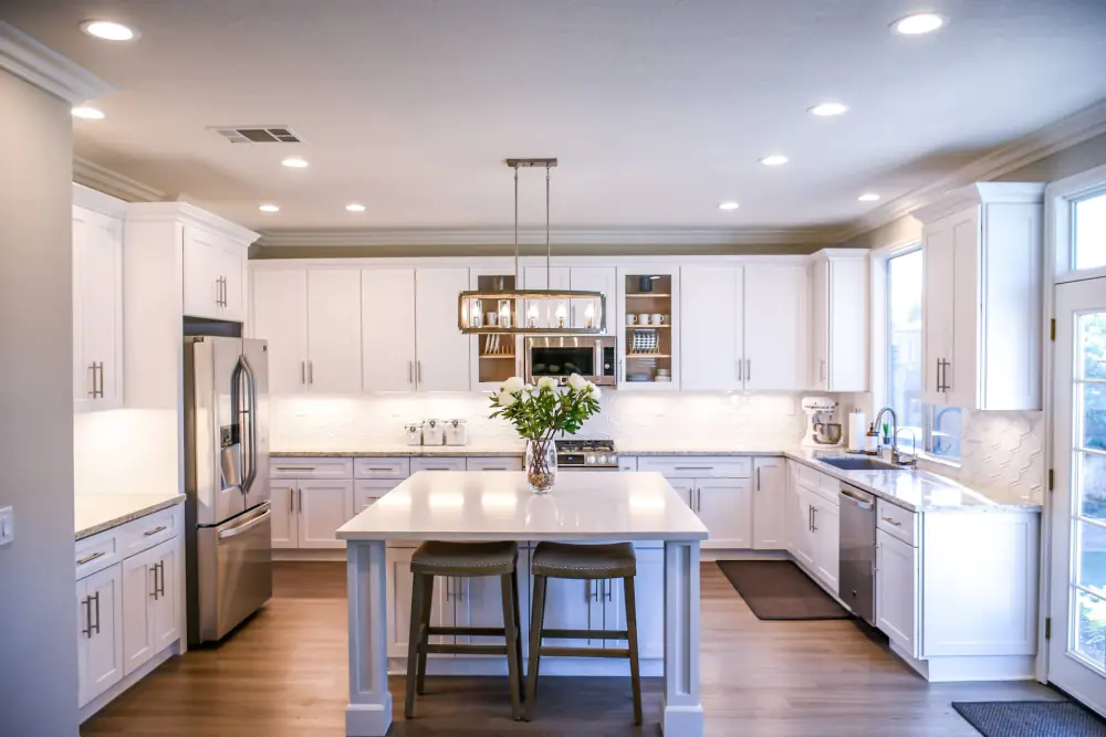 A finished white inset kitchen with a marble-topped island, open shelving and pendant lighting
