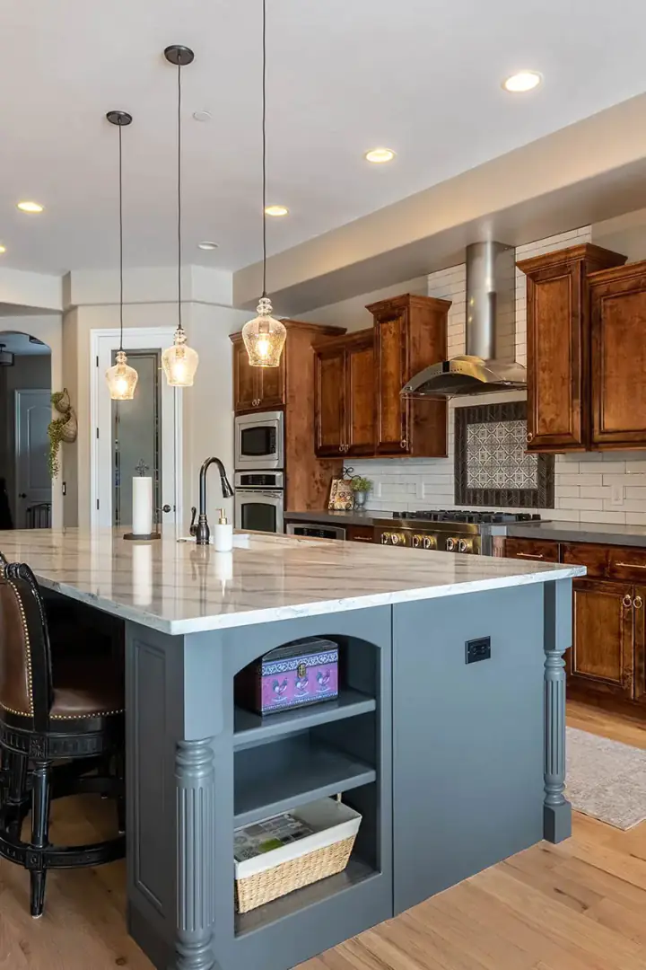 Kitchen with stained white oak perimeter cabinets and a deep blue painted island under pendant lights