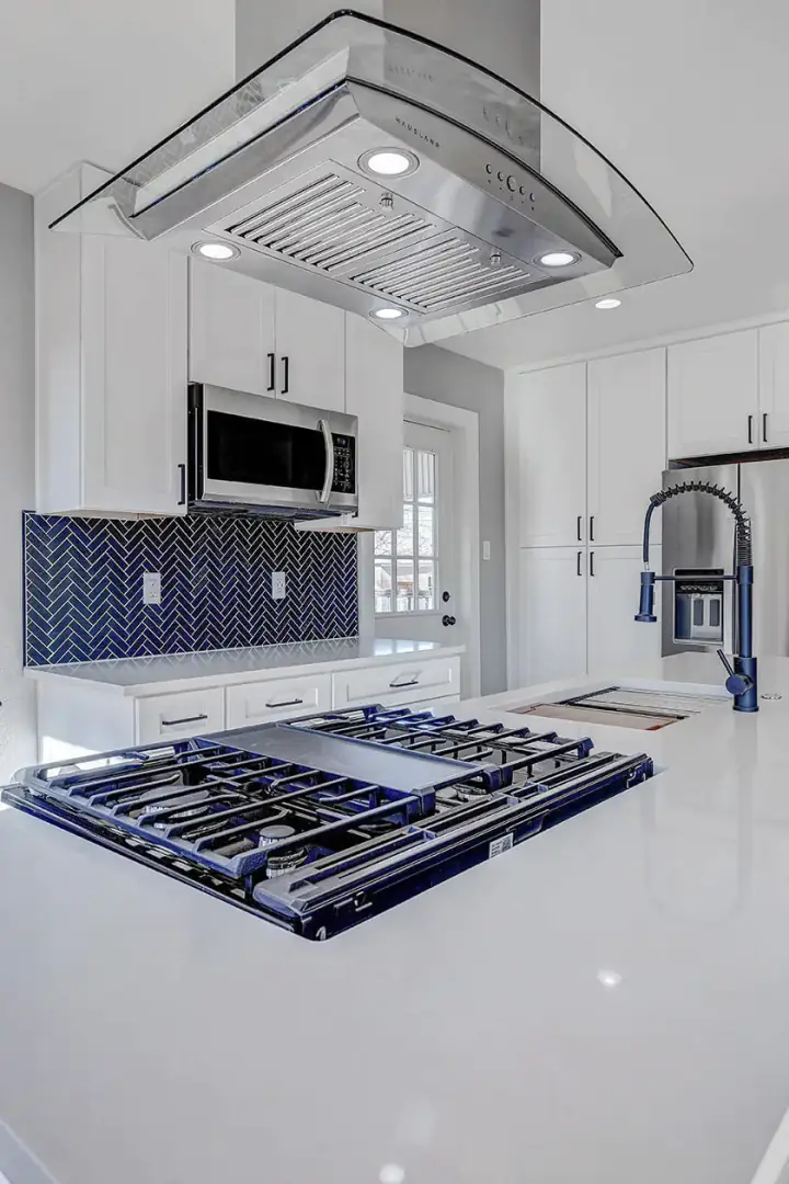 White inset kitchen with a navy herringbone backsplash and a cooktop set into a waterfall quartz island
