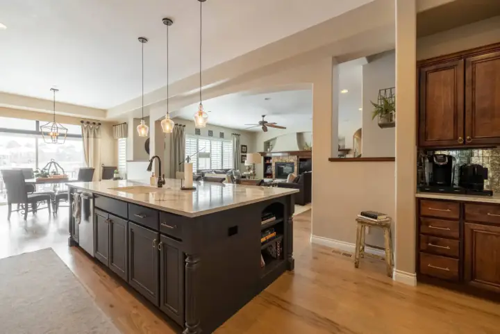 Large charcoal kitchen island with a marble top, pendant lights above, open to a family room